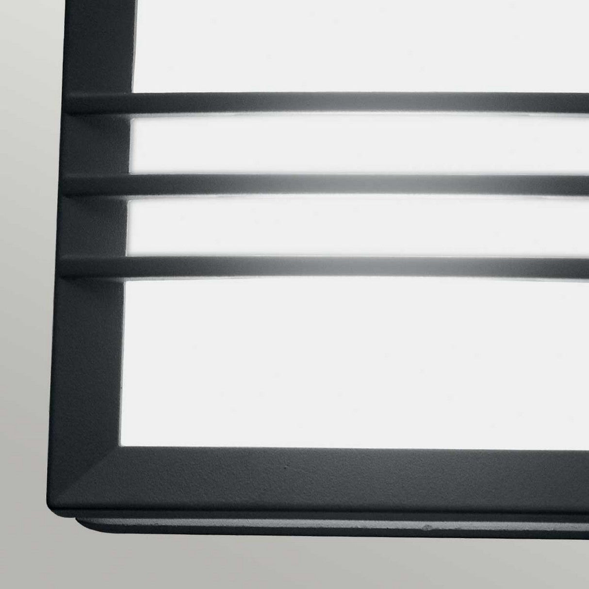 Close-up of the Egil-2 Outdoor Wall/Ceiling Light in graphite, featuring a minimalist design with horizontal metal slats, crafted from cast aluminum. Mounted against a light gray wall, this fixture highlights sleek lines and emits a soft, diffused white light.