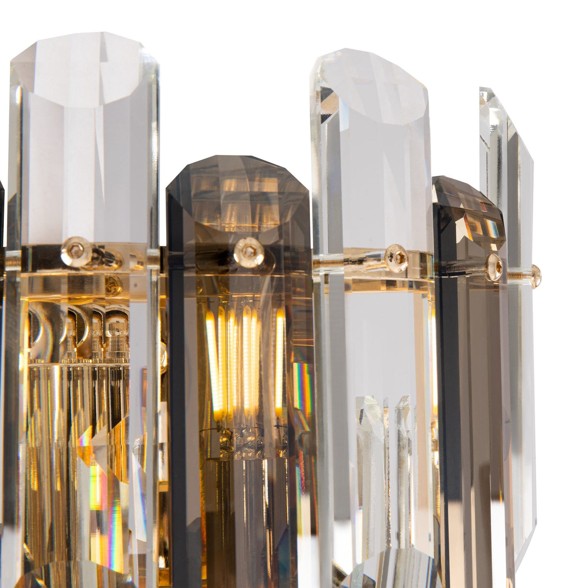 The Flare 2 Light Wall Light in gold, featuring clear and smoky crystals, showcases a modern design with vertical rectangular prisms. The internal bulb emits a warm glow, casting multicolored reflections from its elegant crystal elements.