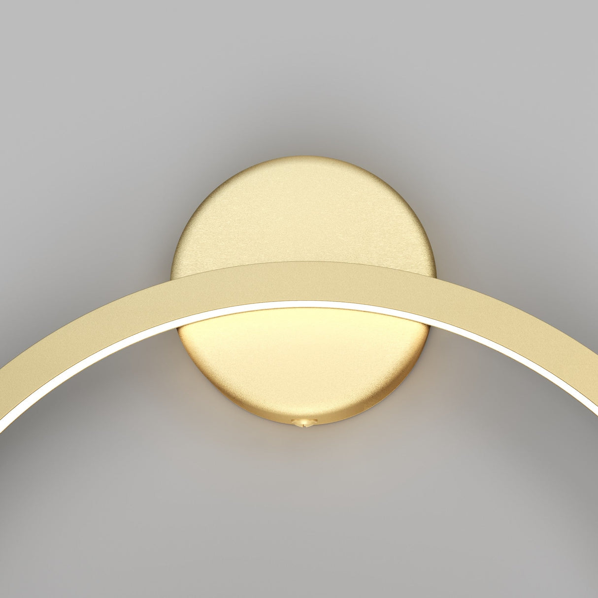 Close-up of the Halo LED Small Ring Wall Light 24W 4000K - Brass, showcasing a circular brass base and an illuminated arching gold arm. Its energy-efficient LED glow contrasts with the plain gray background, enhancing its sleek minimalist design.