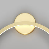 Close-up of the Halo LED Small Ring Wall Light 24W 4000K - Brass, showcasing a circular brass base and an illuminated arching gold arm. Its energy-efficient LED glow contrasts with the plain gray background, enhancing its sleek minimalist design.