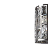 The Gelid Wall Light, featuring a chrome frame and geometric crystal-like panels, illuminates its clear, faceted surfaces to create a sophisticated and elegant appearance against a plain white background.