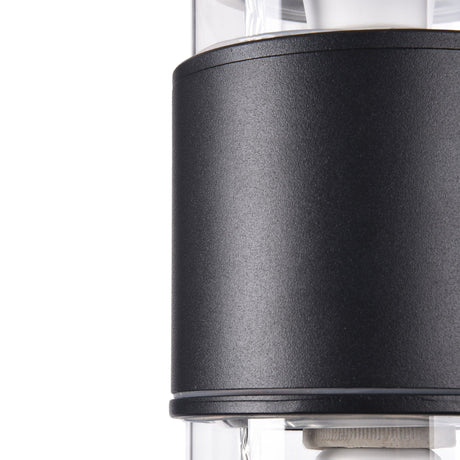 The Bronx Outdoor 2 Light Wall Light in black features a modern, sleek cylindrical design. Its dual-light structure enhances the minimalist allure, contrasting black and transparent elements that reveal metallic components inside.