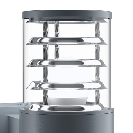 The Bronx Outdoor 2 Light Wall Light - Grey is modern and sleek, featuring a cylindrical design with a frosted glass cover encased in metal rings, providing a minimalist aesthetic with its softly glowing bulb.