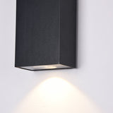 The Times Square Outdoor Wall Light 3000K 6W in black is a wall-mounted rectangular fixture with modern LED lighting, casting a warm glow on white walls. Its sleek design and downward-facing bulb bring contemporary elegance to any space.