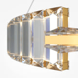 A luxurious chandelier with clear, rectangular segments framed in gold casts reflections. This LED fixture, resembling the Krone LED Circular Crystal Suspension Light 62cm - Gold, is suspended against a white background, highlighting its sleek and elegant design.