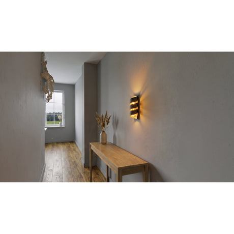 Elizondo Wall Light in black and gold steel, its spiral ribbon design glowing warmly on a hallway wall above a wooden console table.