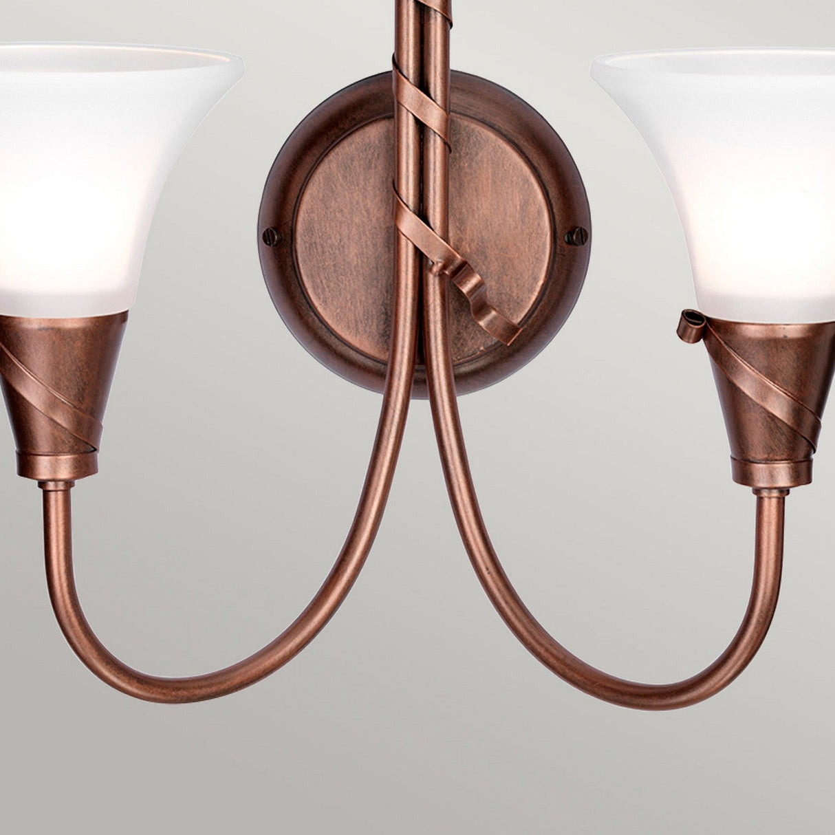 The Emily 2 Light Wall Light - Copper Patina showcases upward-facing frosted glass shades on a bronze fixture. With its symmetrical design, elegant curved metal arms, and round backplate, it offers a classic and stylish look.