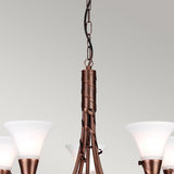 A close-up of the Emily 5 Light Chandelier - Copper Patina highlights its vintage charm with frosted glass shades. The fixture is adorned with intricate twisted metal detailing and includes a hanging chain, all finished in a copper patina. The background is light gray.