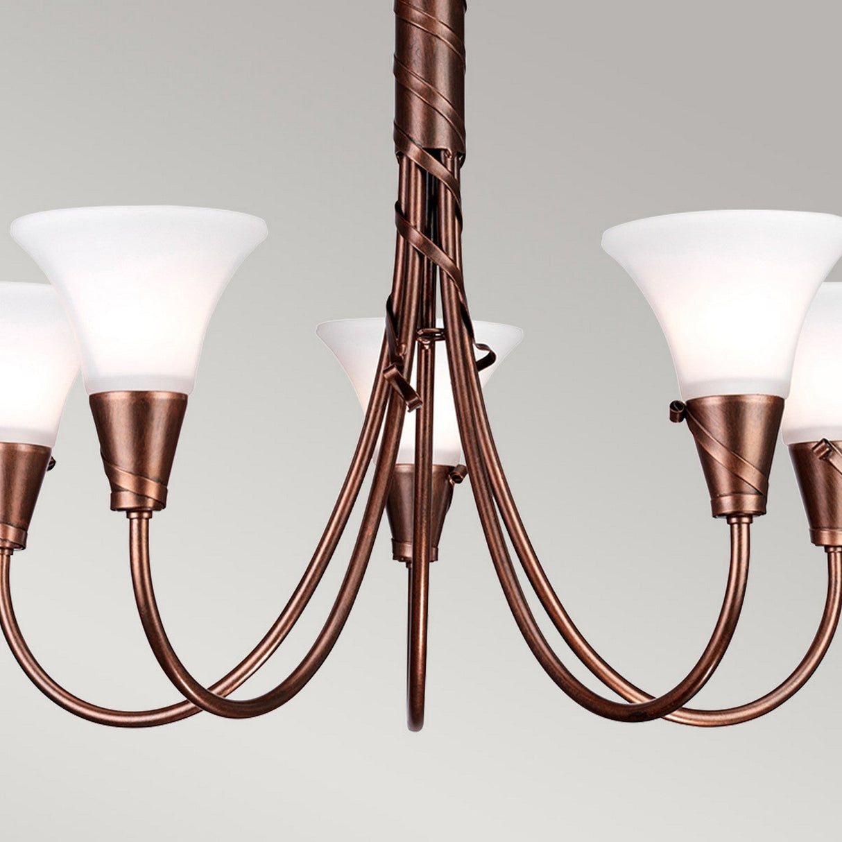 The Emily 5 Light Chandelier - Copper Patina features a copper patina finish with five upward-facing frosted glass shades and elegantly curved arms, offering a vintage appeal in its simple, modern design against a light gray backdrop.