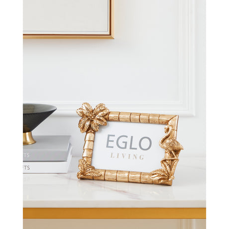 Gold Esashi Photo Frame with bamboo-effect border, palm tree and flamingo detailing, displayed on a marble console beside books and a dark bowl.