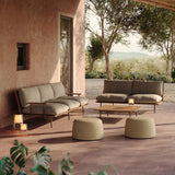 Two round Esen upholstered outdoor pouffes in beige fabric with tapered drum shapes, shown on a terrace beside matching sofas and a wooden coffee table.