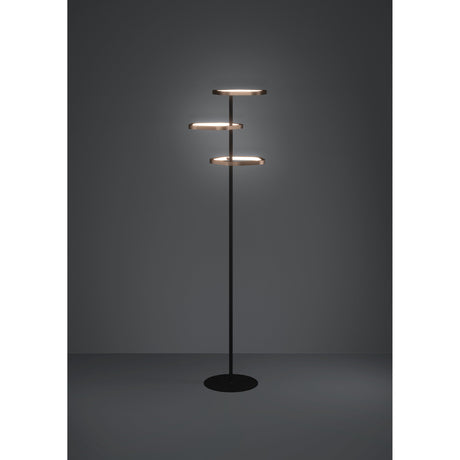 Estrella LED floor lamp with three bronze-ringed disc heads at staggered heights on a slim black steel stem and round black base, shown against a dark grey background.