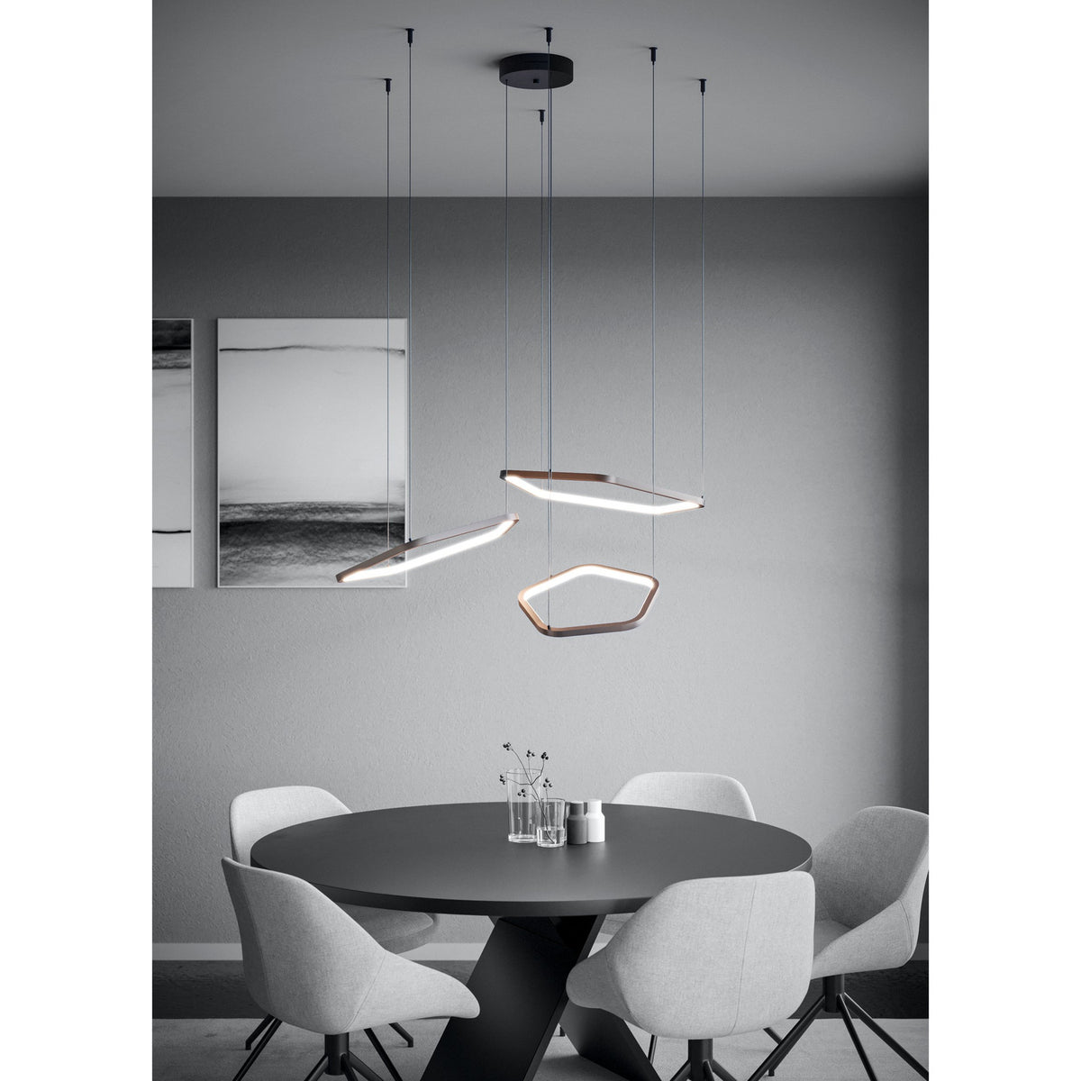 Estrella Pendant Light with three bronze hexagonal LED rings at varied heights from a black ceiling canopy, shown above a round dining table in a grey room.