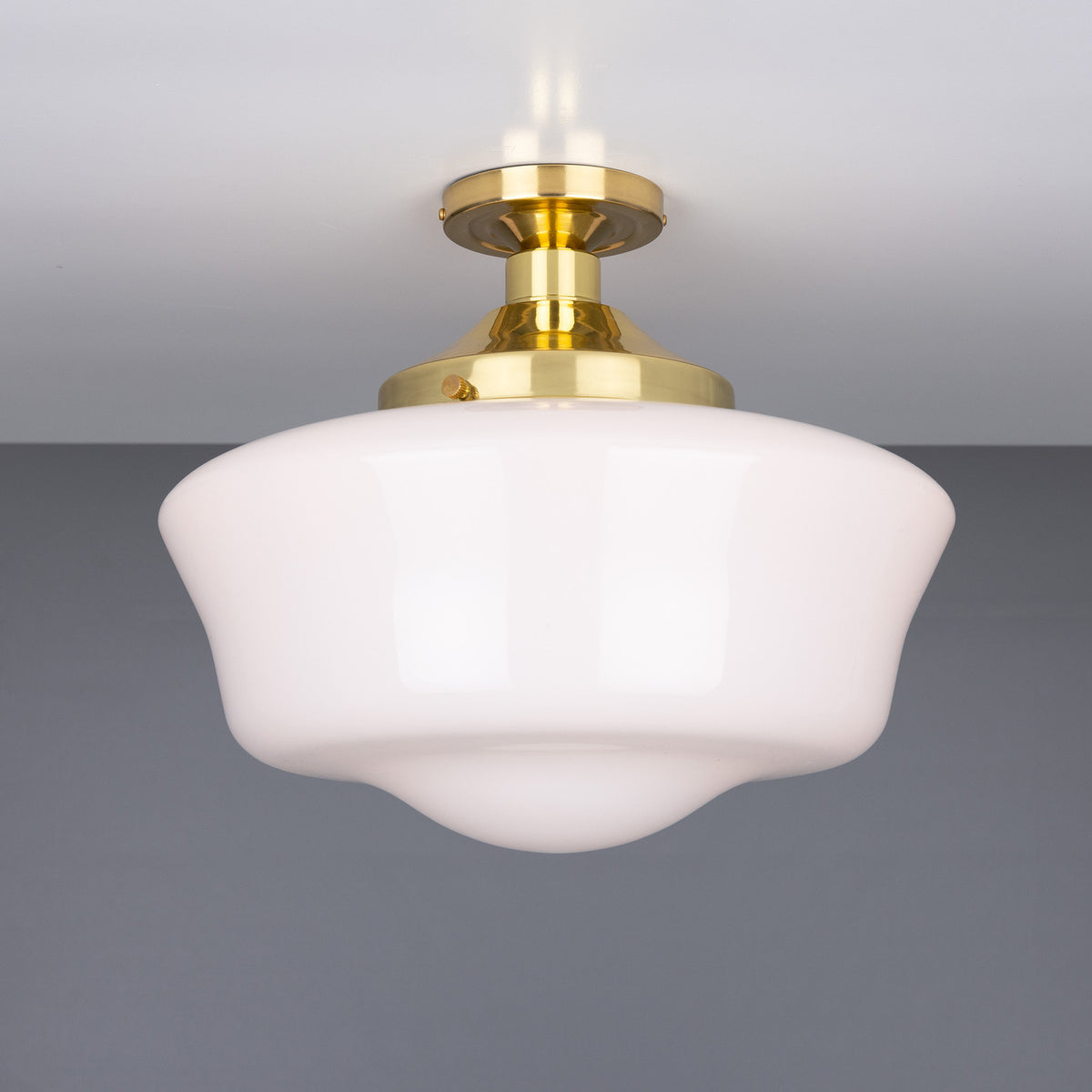Ethrina Glass Semi Flush Ceiling Light with white opal schoolhouse-style glass shade and polished brass fitter, mounted close to the ceiling on a round brass plate against a plain grey background.