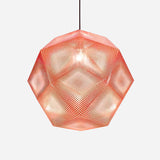 The Rango Large Pendant Light - Copper showcases a perforated dodecahedron design with a red surface, suspended by a black cord to cast a warm glow. Its acid-etching technique enhances the intricate, mesh-like effect against its white background.