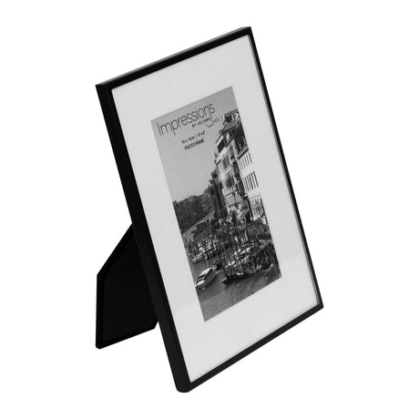 Matt black metal photo frame with white mount, holding a 6 x 4in print, shown at an angle on a plain white background with easel stand visible.