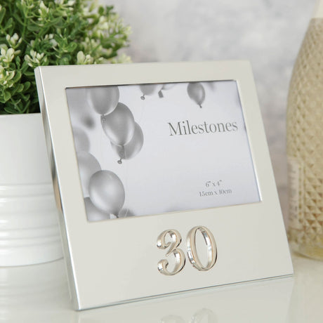 Silver aluminium 6x4in photo frame with raised 3D "30" below the picture, shown on a table beside a plant and candle.