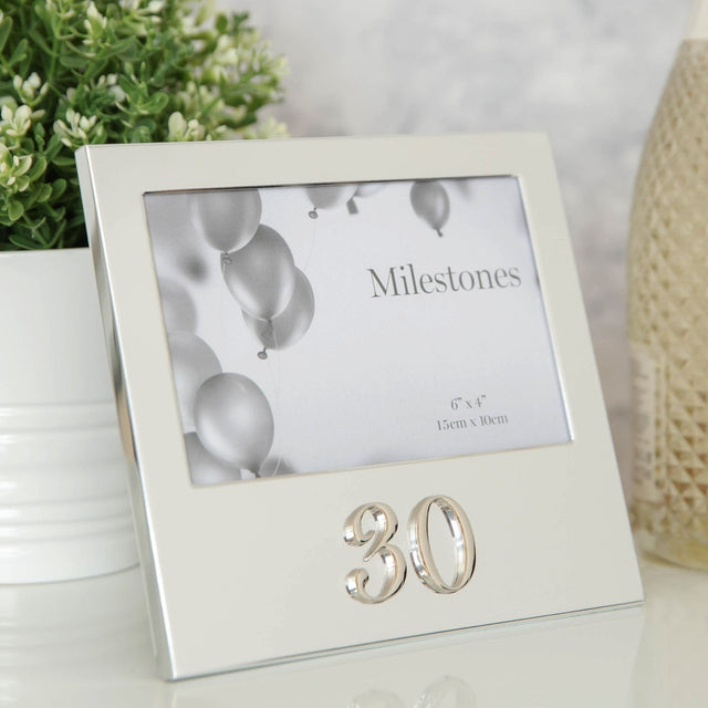 Silver aluminium 6x4in photo frame with raised 3D "30" below the picture, shown on a table beside a plant and candle.