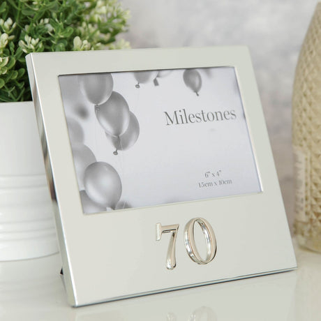 Silver aluminium 70th birthday photo frame with raised 3D "70" numbers below a landscape 6 x 4in opening, shown beside a potted plant.