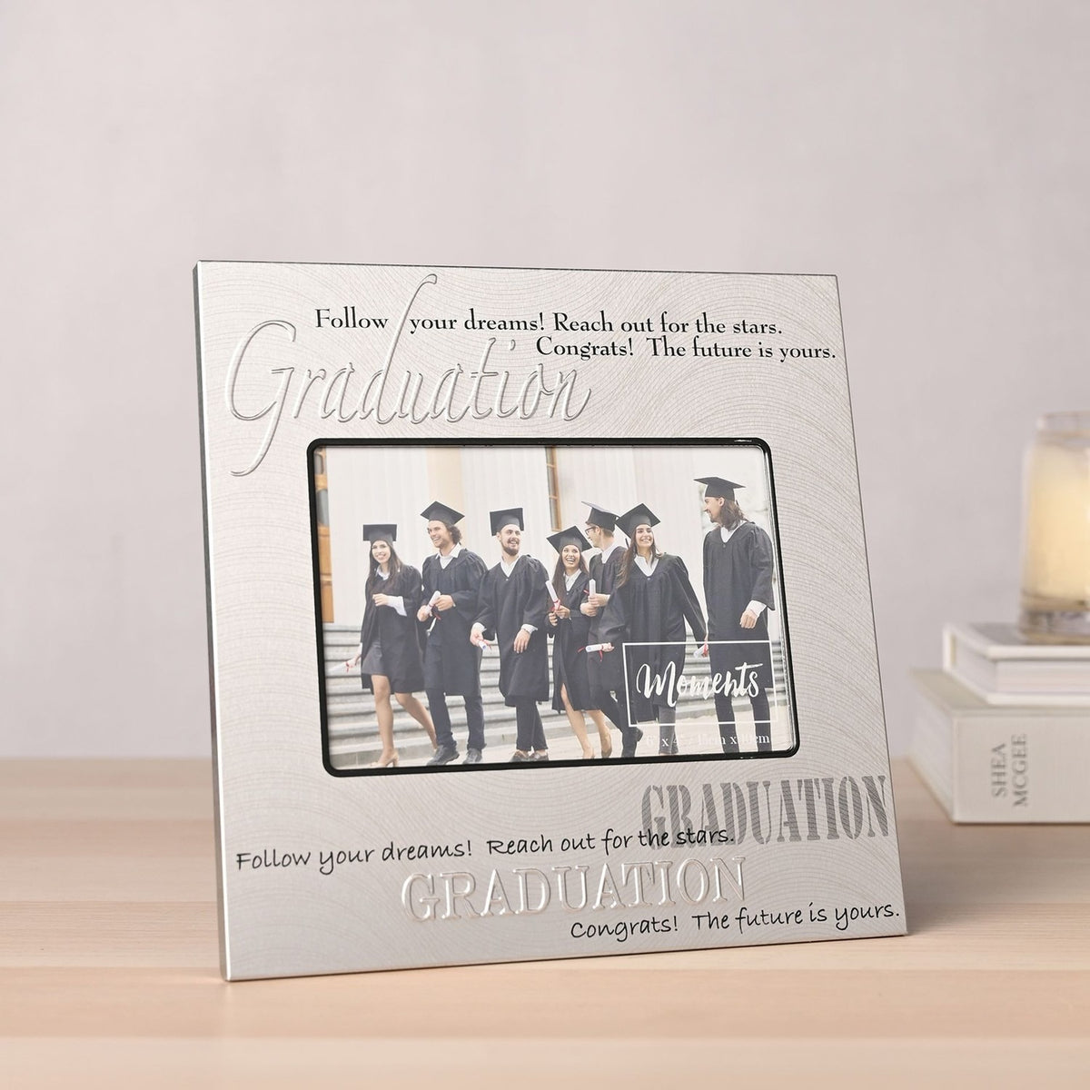 Square satin silver aluminium photo frame with embossed "Graduation" text and inspirational quotes, holding a 6x4in photo of graduates, displayed on a wooden surface.