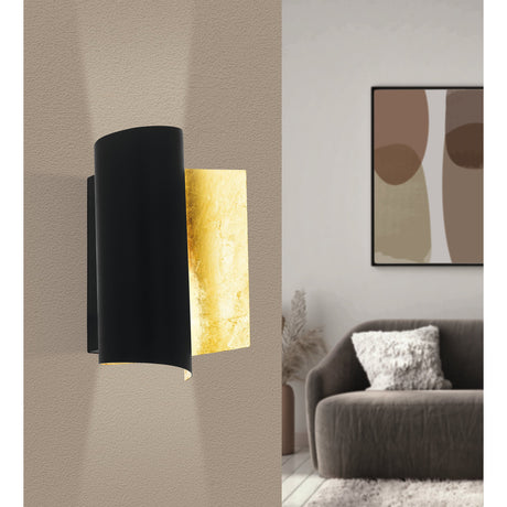 Falicetto Wall Light in black and gold, steel wall fixture with curved matt black shade over a crinkled gold back plate, shown on a beige wall beside a living room with sofa and framed art.