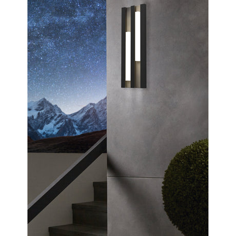Fandina LED Outdoor Wall Light in black, a tall ribbed panel with two vertical white light bars, mounted on a grey exterior wall at dusk.