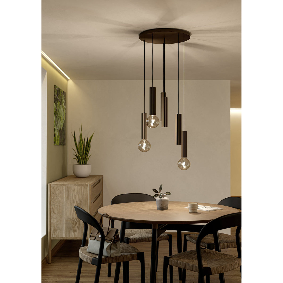 Fariolo 6 Light Pendant in bronze with ribbed steel tubes at staggered heights from a round ceiling plate, shown above a round wooden dining table.