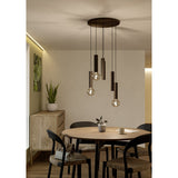 Fariolo 6 Light Pendant in bronze with ribbed steel tubes at staggered heights from a round ceiling plate, shown above a round wooden dining table.