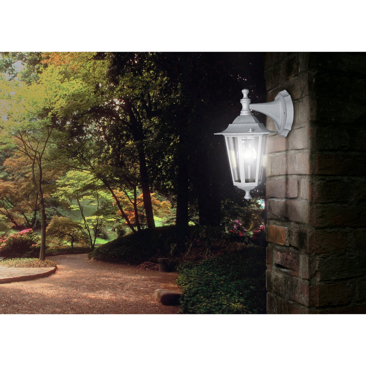 Fasvette Downward Outdoor Wall Light in white, a six-sided cast aluminium coach lantern with clear glass panels on a curved bracket, mounted on a stone pillar in a garden setting.