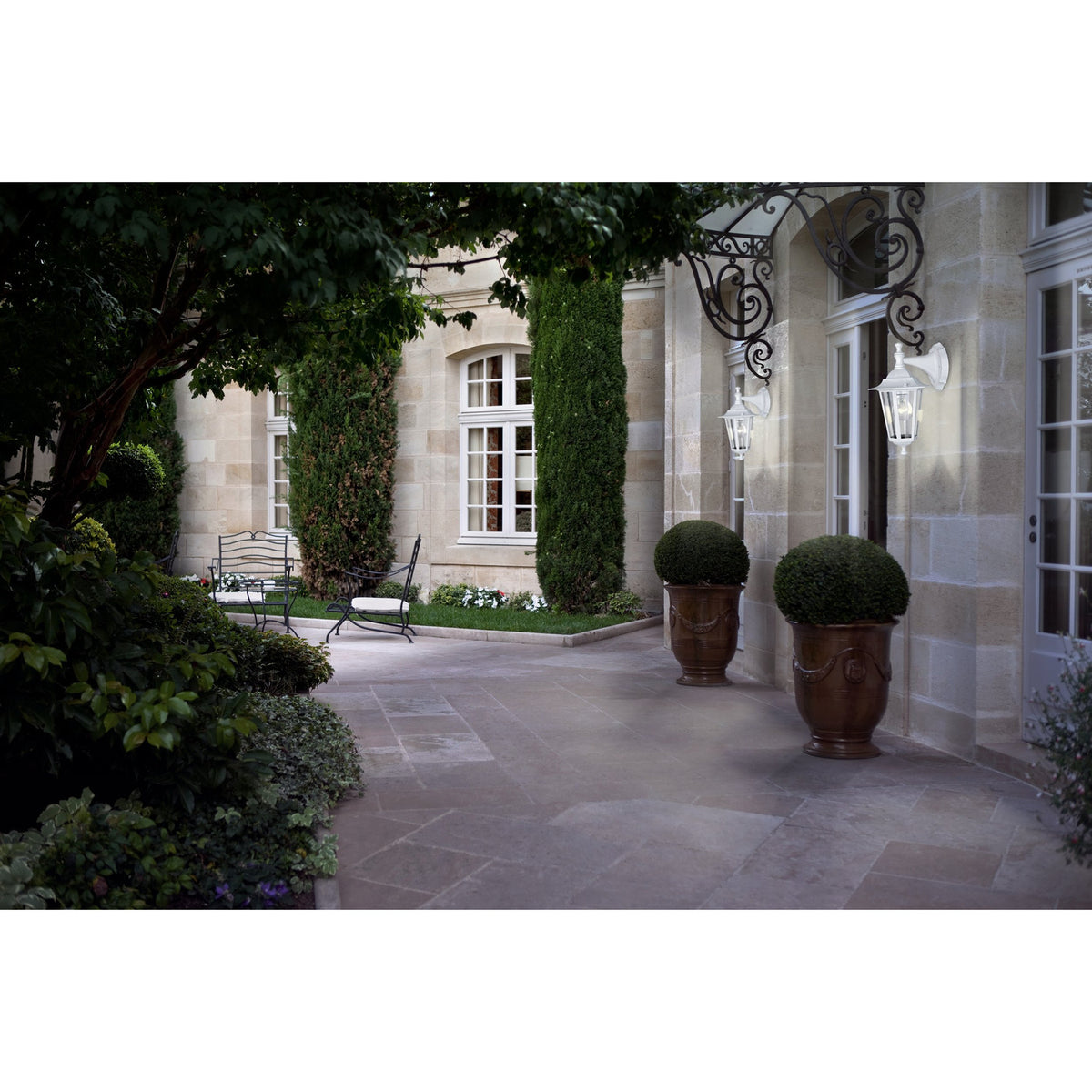 Fasvette Downward Outdoor Wall Light in white cast aluminium with glass panels, mounted on a stone façade beside French doors in a courtyard setting.