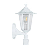 Fasvette white traditional six-sided lantern outdoor wall light with clear glass panels, cast aluminium body, curved wall bracket and motion sensor, shown on a plain white background.