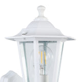 Close-up of the Fasvette white cast aluminium outdoor wall light, a six-sided lantern with clear glass panels, visible motion sensor, and E27 bulb, shown against a plain background.