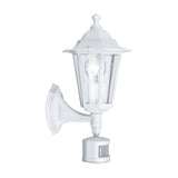 Fasvette white cast aluminium outdoor wall light, six-sided lantern with clear glass panels, visible bulb, curved wall bracket and motion sensor, shown on a plain white background.