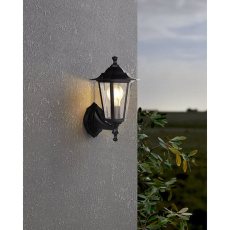 Fasvette Upward Outdoor Wall Light in black cast aluminium with clear glass panels, lit E27 bulb, mounted on a textured grey exterior wall.