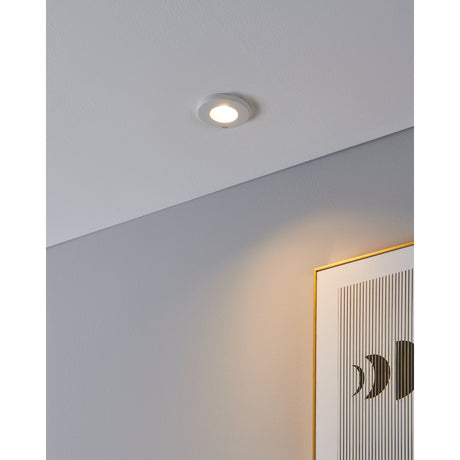 Favazzina 8.5cm round recessed downlight in white steel with clear glass cover, installed on a white ceiling casting warm light onto a hallway wall beside a framed print.