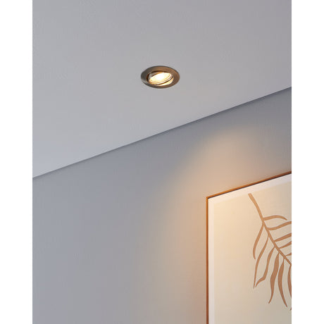Favazzina recessed downlight in satin nickel with tiltable inner ring, shown fitted into a grey ceiling and casting warm white light onto a framed print below.