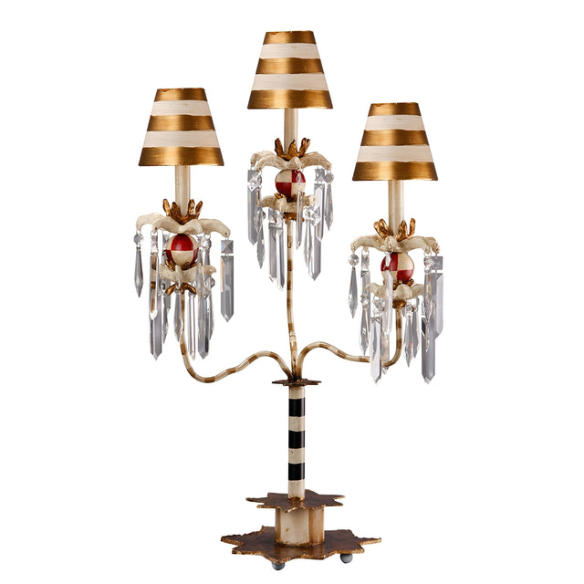 Introducing the Birdland 3 Arm Table Lamp - Cream & Gold, featuring a whimsical and artistic candelabra-style design. This decorative lamp comes with striped gold and white shades, accented by hanging K9 cut glass clusters and ornate red details. The lamp elegantly blends metal and crystal elements to create an eye-catching piece.