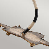 A close-up of the Dominique 1 Light Table Lamp showcases its modern, decorative metal sculpture design with an uneven, textured base. The lamp features a curved rod adorned in black and cream stripes extending upwards, while the base is highlighted by a rustic gold leaf finish against a plain light gray background.