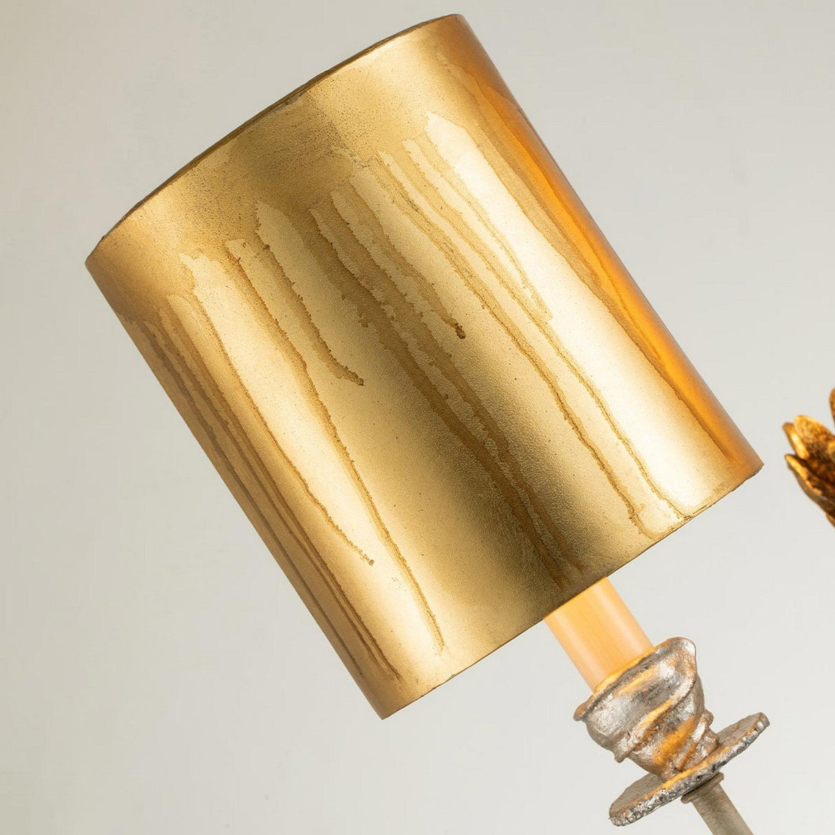 A close-up of the Flambeau 2 Light Wall Light features a golden metal lampshade with vertical streak patterns, enhanced by gold and black details, and mounted on a decorative metal stand. The softly blurred background highlights its shiny surface reminiscent of a Mardi Gras design.