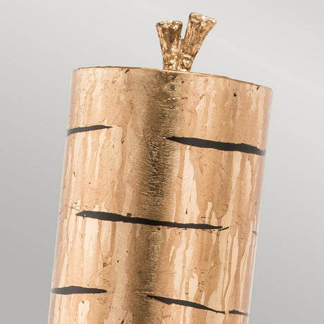 The Fragment 1 Light Wall Light - Aged Gold boasts a cylindrical design that mimics a tree trunk with its textured finish, complemented by black horizontal lines. The top of the light features two small protrusions resembling branches, offering a blend of modern and vintage aesthetics against a plain light gray background.