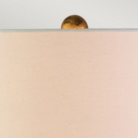 A close-up of the off-white, rectangular lampshade on the Gallier 1 Light Table Lamp - Black & Gold, showcasing a round, golden metallic finial at the top against a blurred gray background. This elegant piece of home decor is beautifully accented with sleek touches of black and gold.