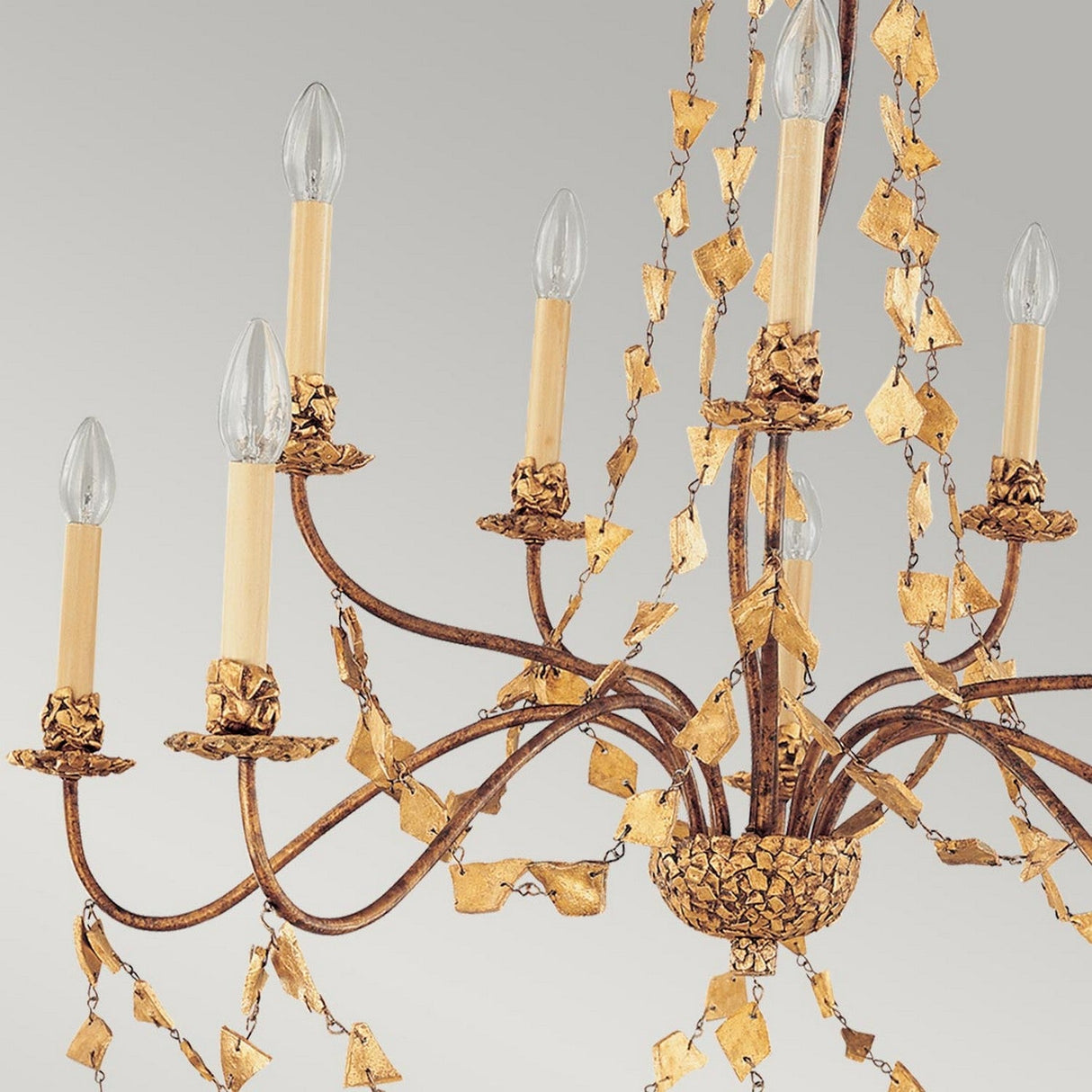 A detailed view of the Mosaic 10 Light Chandelier - Gold, showcasing a luxurious golden finish with multiple arms and candle-shaped bulbs. Delicate gold leaf decorations adorn the arms, enhancing its sophisticated appearance with intricate mosaic-inspired designs.