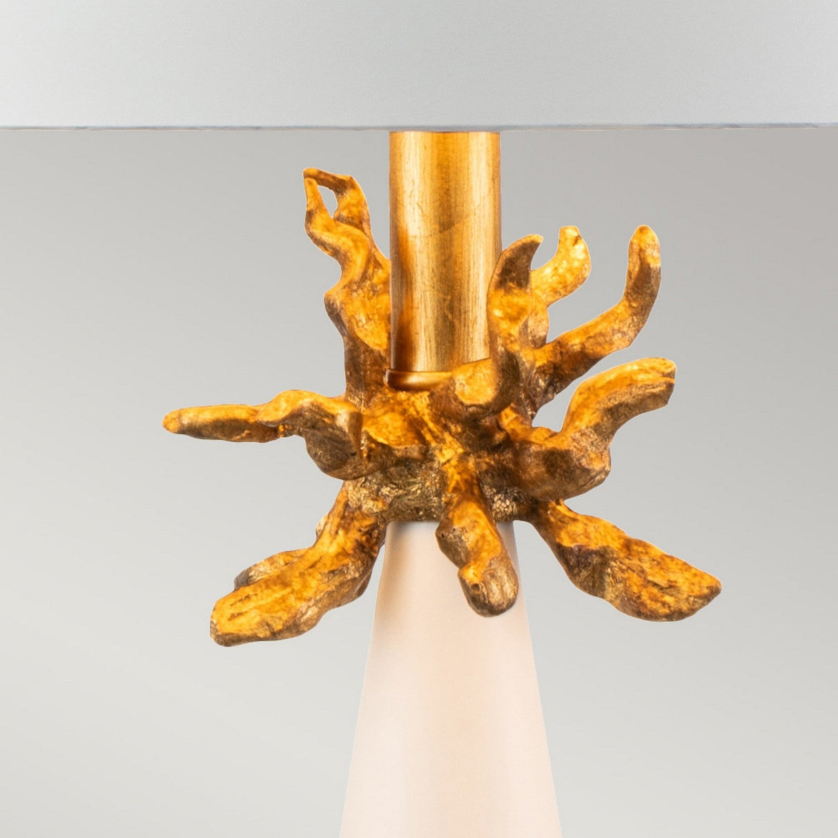A close-up of the Neo 1 Light Table Lamp - White & Gold base highlights a sleek, modern design with a golden, tree-like motif encircling the center. The lamp features metal construction with Gold Leaf accents, set against a neutral background to accentuate its elaborate detailing.
