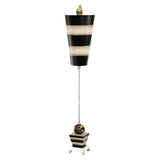 The Peony 1 Light Table Lamp showcases a tall, abstract design decorated with black and taupe stripes. It features a narrow top and broader base, accented by small golden details at both ends connected by a slender vertical rod. This elegant piece stands on a silver leaf-finished four-legged platform.