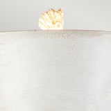 A small, irregularly shaped piece of beige and brown coral rests on the edge of a Petra 1 Light Table Lamp - Bone White's smooth, curved surface against a plain background. The cracked texture of this contemporary design creates a striking contrast with the coral.