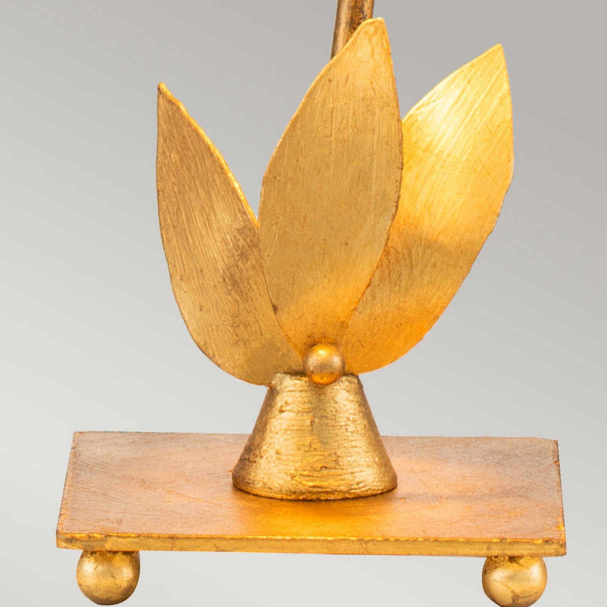 A golden abstract sculpture showcases three textured, nature-inspired leaf shapes extending upwards from a conical base, resting on a rectangular platform with Gold Leaf accents and small spherical supports against a neutral backdrop. It pairs beautifully with the Red Bell 1 Light Table Lamp - Gold Leaf.