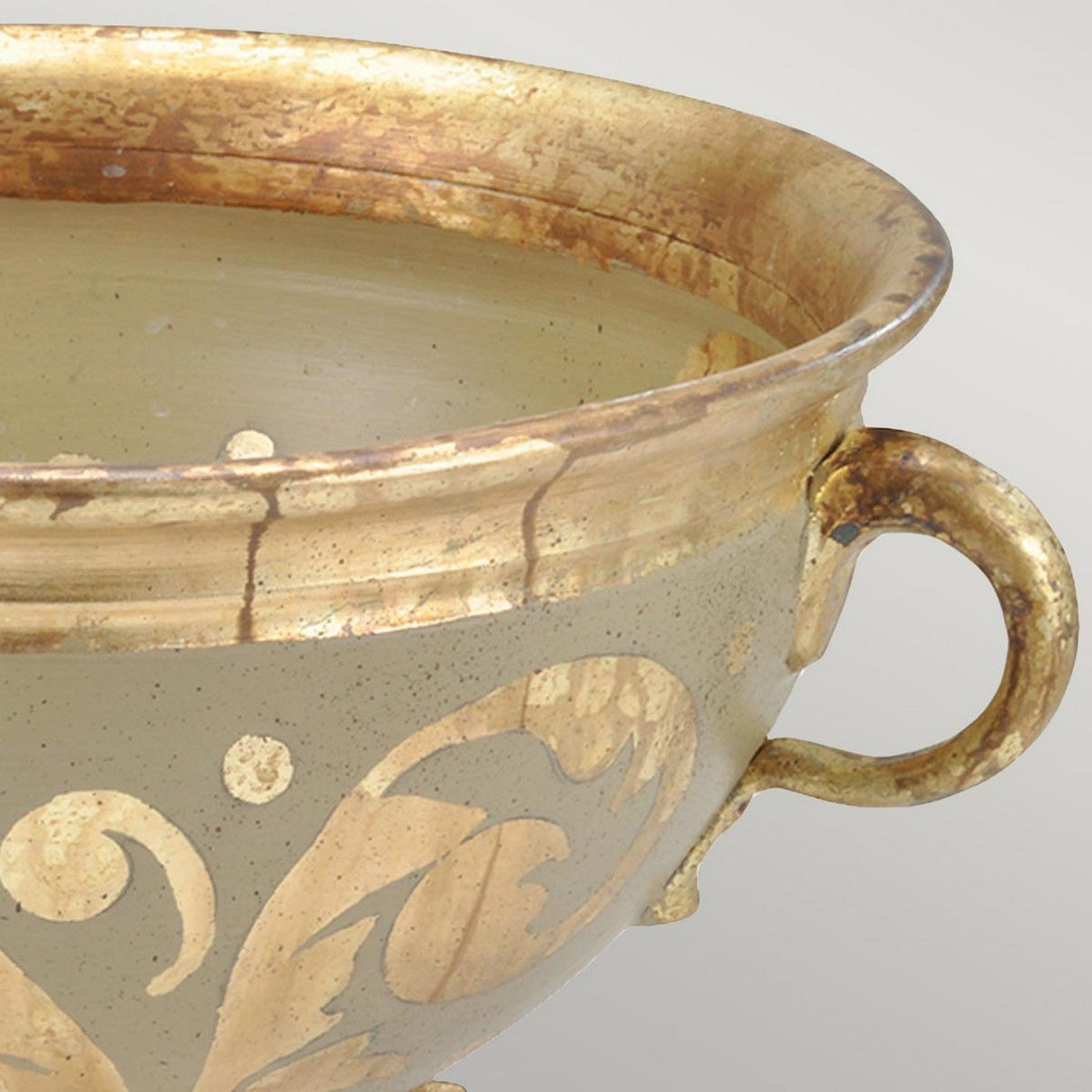 Close-up of the Rocheblave Decorative Bowl, featuring an ornate design with an antiqued gold leaf finish and a decorative handle. Intricate etched designs embellish the brass, complemented by a weathered patina that enhances its vintage allure. The simple, neutral gray background highlights its charm as a stunning piece of interior decor.