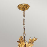 The Sweet Olive 3 Light Chandelier – Gilded Gold hangs elegantly, featuring a crystal medallion and leaf-shaped accents, against a light gray background.
