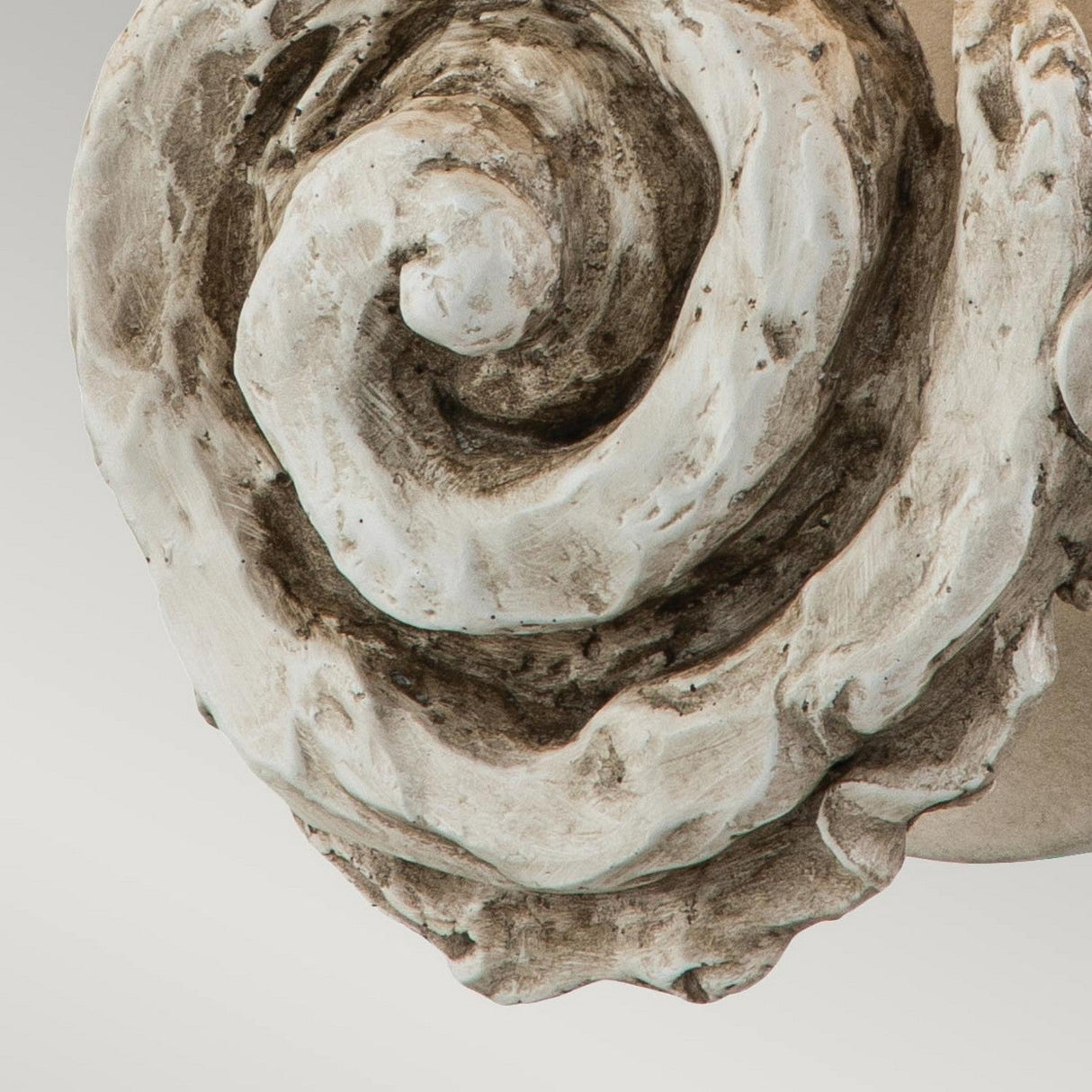 A close-up of the Swirl 1 Light Large Wall Light reveals a carved spiral design with textured swirls and a weathered look. The stone exhibits a blend of white and brown shades, enhancing its intricate details and capturing the elegance and charm of classic artistry for any space.