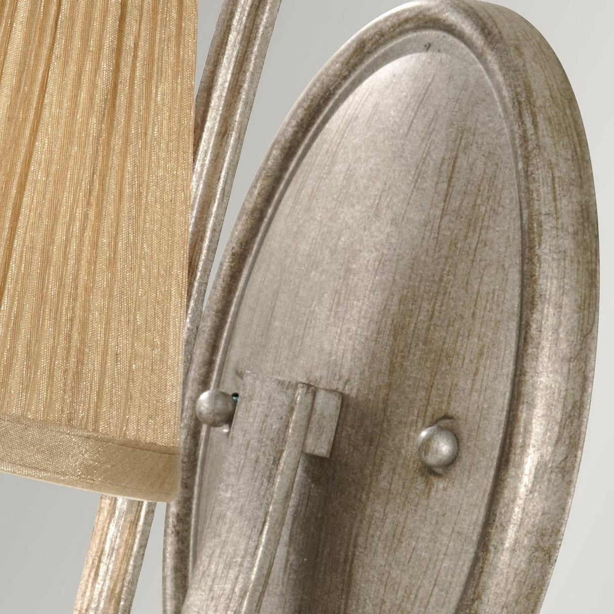 Close-up of the Abbey 1 Light Wall Light in Silver Sand, showcasing its textured metallic design with a ribbed, beige fabric shade. The oval metallic backplate features a Silver Sand finish with subtle weathered detailing, imparting a vintage charm to the design.